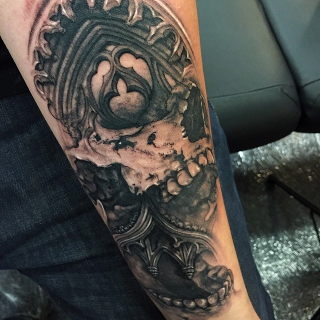 Terrifying black ink forearm tattoo of human skull with building