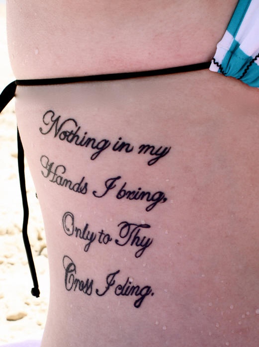 Tatuaggio sul fianco il testo &quotNOTHING IN MY HANDS I BRING ONLY TO FLY CROSS I CLING "