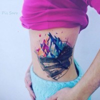 Tatuaje en el costado,  pila de libros con montañas de varios colores
