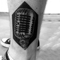 Tatuaje en el tobillo, 
micrófono  gris en el fondo negro