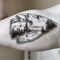3D like nice colored ancient arrow head tattoo on biceps stylized with mountains and forest