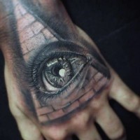 3D like very detailed human eye tattoo on hand combined with big pyramid