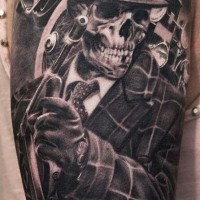 Tatuaje en el brazo, cráneo sonriente de mafioso con arma