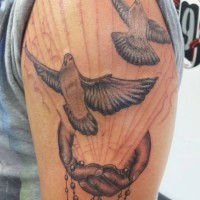 Schwarzweisses Tattoo mit Tauben , Händen und Perlenschmuck am Oberarm