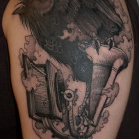 Cartoon black-and-white raven with gramophone in clouds tattoo on upper arm
