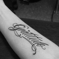 Curled gratitude word tattoo on forearm