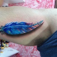 Cute bright blue-colored feather tattoo on arm