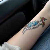 Tattoo mit blauen Vögelchen, kleinen Blümchen und feinem Aufschrift am Arm