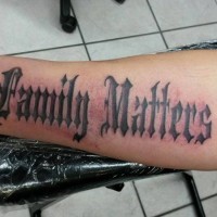 Great gothic-lettered family matters quote tattoo on forearm