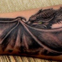 Large black green-eyed dragon tattoo on forearm