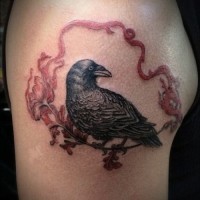 Realistic raven sitting on flower with red ribbon tattoo on upper arm