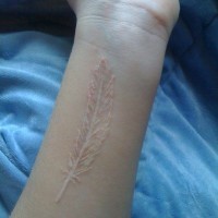 Tender long white-contour feather tattoo on wrist
