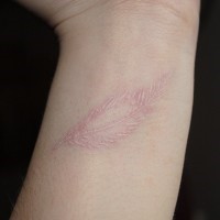 Tender white-contour feather tattoo on wrist