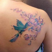 Tatuaje en el omóplato,  pájaro azul gracioso  con flores, colores suaves