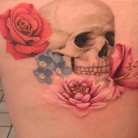 Accurate pained and colored human skull tattoo on thigh with various multicolored flowers