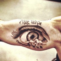 Tatuaje en el brazo, ojo terrorífico con dedos y inscripción