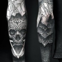 Tatuaje en el antebrazo, cráneo humano oscuro con ornamentos diferentes y flores