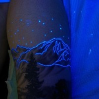 Tatuaje en el brazo, montañas encantadores con estrellas, tinta ultravioleta