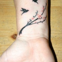 Tatuaje en la muñeca,
dos aves negras y  ramita con flores