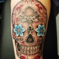 Tatuaje en el antebrazo, calavera de azúcar con dos flores azules