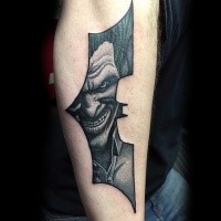 Batman symbol shaped black ink arm tattoo stylized with smiling Joker