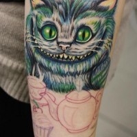 Tatuaje en el antebrazo,
gato de Cheshire sonriente adorable con taza de té y magdalena