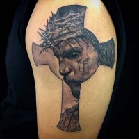Big antic like cross tattoo on shoulder stylized with detailed sad Jesus portrait