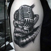 Tatuaje en el brazo, micrófono vintage con la mano y teclas del piano