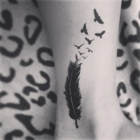 Birds flying from feather black ink tattoo on ankle
