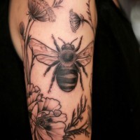 Tatuaje en el brazo, abeja  entre flores de colores gris y negro