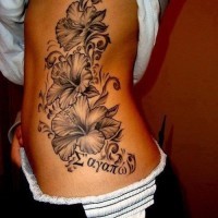 Black and gray hibiscus flowers and inscription tattoo on ribs