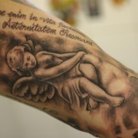 Tatuaje en el brazo en negro y gris de angelito sentado