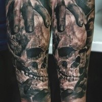 Black and gray style colored forearm tattoo of human hand holding skull