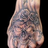 Schwarzer und grauer kleiner gruseliger menschlicher Schädel mit Rosen und Reben Tattoo an der Hand