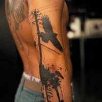 Black flying crow and power line tattoo on arm with lettering and paint drips