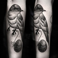Tatuaje de ave con huevo, color gris, en el antebrazo