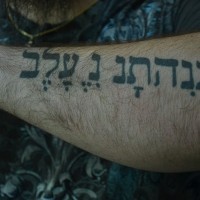 Tatuaje en el antebrazo, frase hebrea, letras grandes
