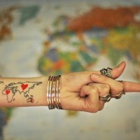 Black ink contour world map with tiny red hearts tattoo on forearm zone