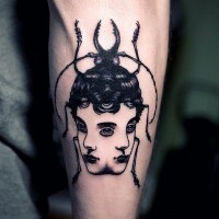 Tatuaje en el antebrazo,
escarabajo negro surrealista con dos caras de chicas