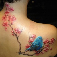 Tatuaje en el hombro, pájarito suave se sienta en la rama