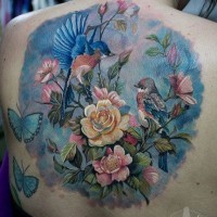 Tatuaje en la espalda,
dibujo en colores pastel de pájaros con flores y mariposas