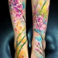 fiori colorati luminosi e fiori rosa su ramo tatuaggio su due gambe