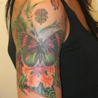 Tatuaje  de mariposa entre flores y hojas y hierba en el brazo
