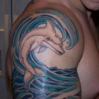 Cartoon like colored little dolphin in waves upper arm tattoo