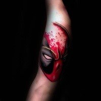 Cartoon style colored arm tattoo of bloody Deadpool head