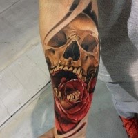 Cartoon style colored arm tattoo of scary human skull and rose