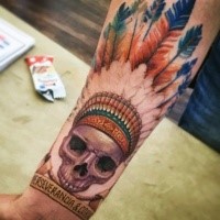 Cartoon style colored forearm tattoo of ancient Indian skull with feather and lettering