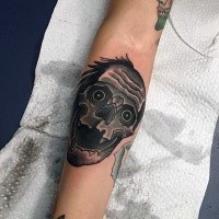 Cartoon style funny looking forearm tattoo of monster skull with blue eyes