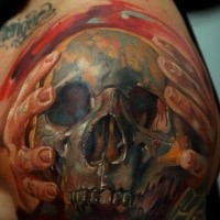 Colored horror style large shoulder tattoo of hands holding human skull