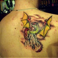 Coloured dragon on a mountain top tattoo on shoulder blade